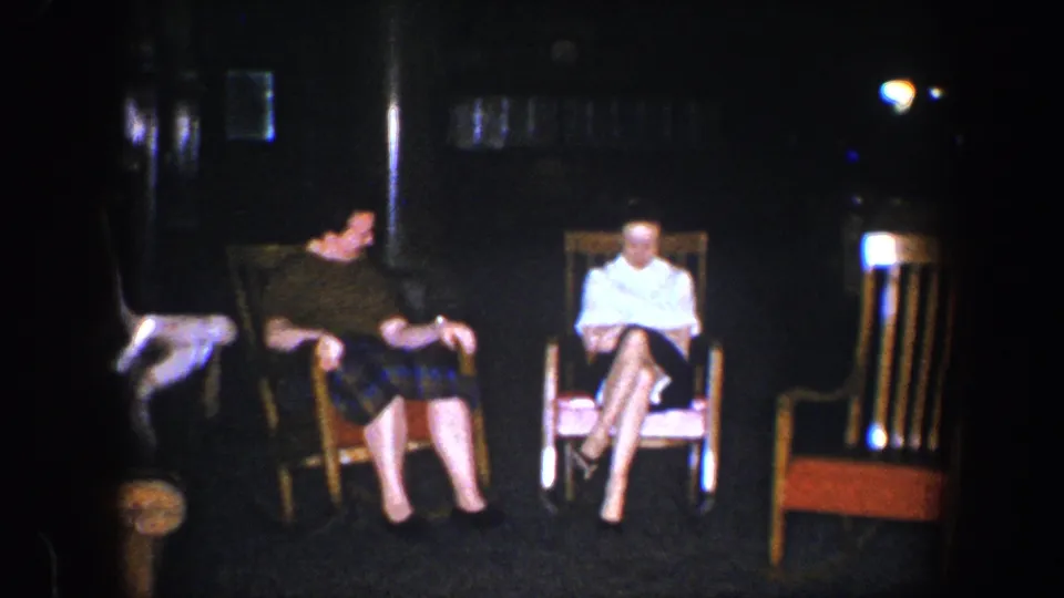 Near the end of the clip, the two women sit quietly in the dim Baltimore interior, framed by wooden chairs and dark walls.