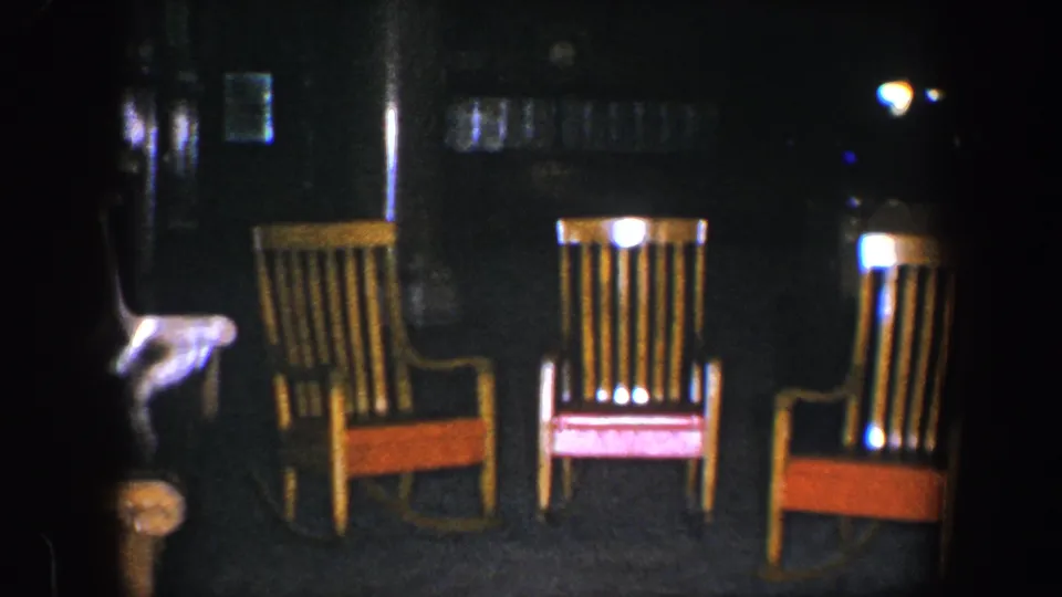After the women leave, the 1960 Baltimore home-movie frame shows empty wooden rocking chairs in the dark interior.