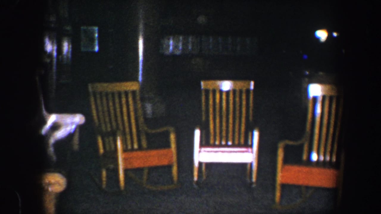 Three wooden rocking chairs with orange seats in a dark room.