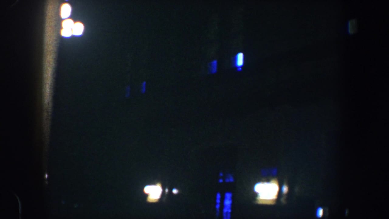 1960 Baltimore night footage showing blurred warm lights and blue window glows across a dark columned building facade.
