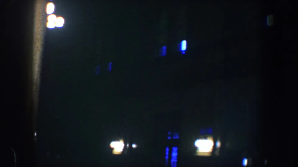 1960 Baltimore night footage showing blurred warm lights and blue window glows across a dark columned building facade.