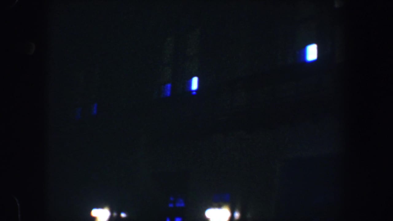 Shadowed building exterior with scattered blue lights and bright low streetlights at night.