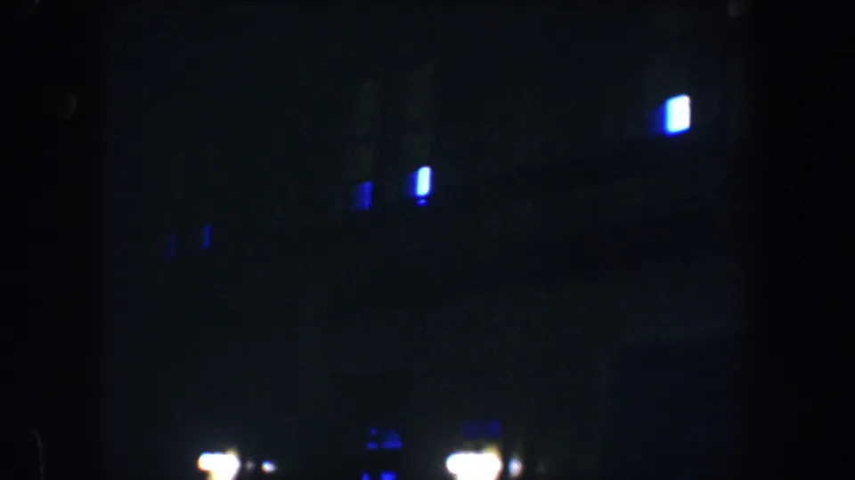 Dark 1960 Baltimore street-level view with scattered blue window lights and bright lamps near a shadowed facade.