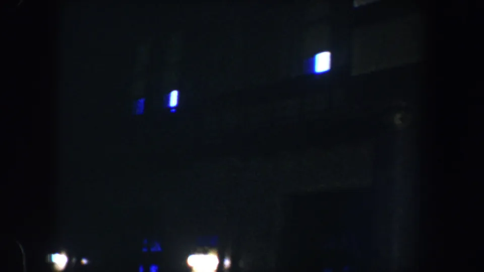 1960 Baltimore night frame with soft blue window lights, bright streetlight glare, and dark column-like vertical forms.