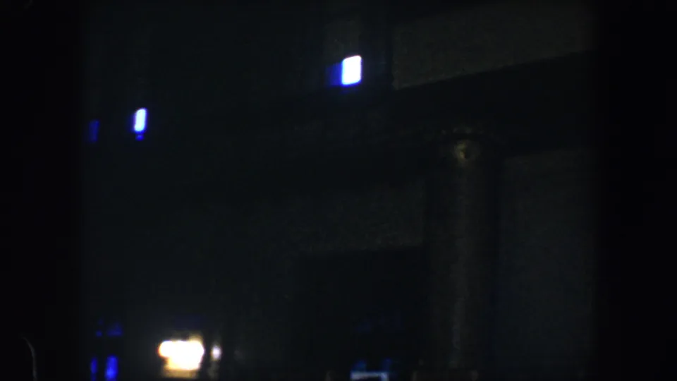 Late frame from a 1960 Baltimore night clip, showing a dark building facade with blue window light and warm streetlight glare.