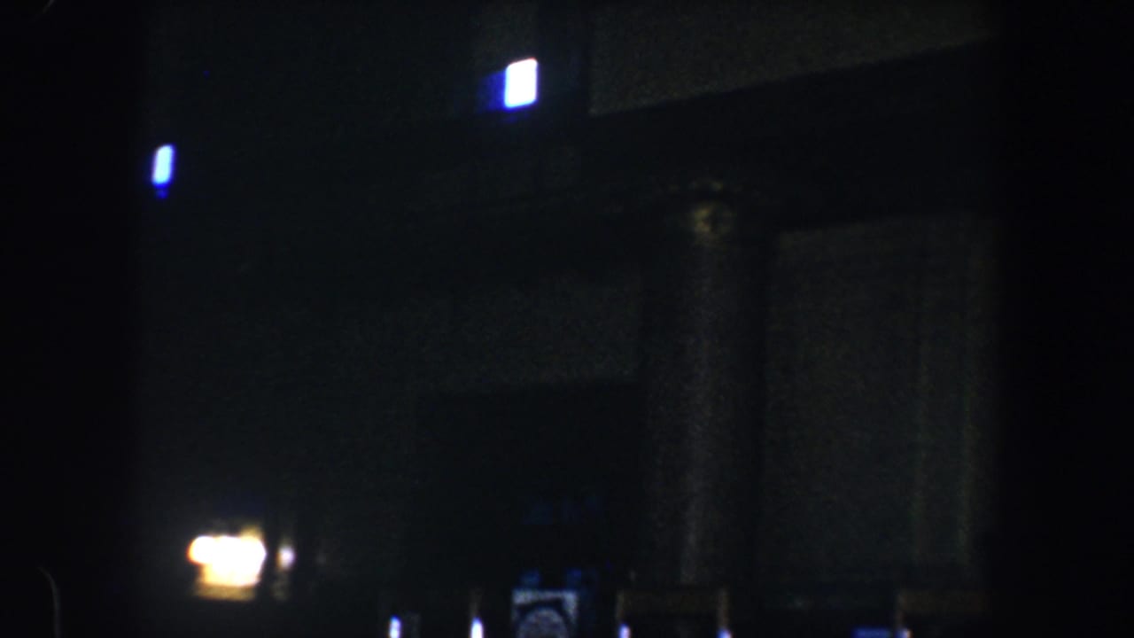 Dark interior with faint lights, columns, doorway, clock, and posted signs.