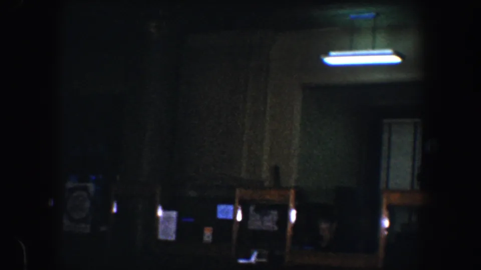 1960 Baltimore 8mm frame showing a darkened interior with a lit doorway area, columns, posted signs, and faint architectural detail.