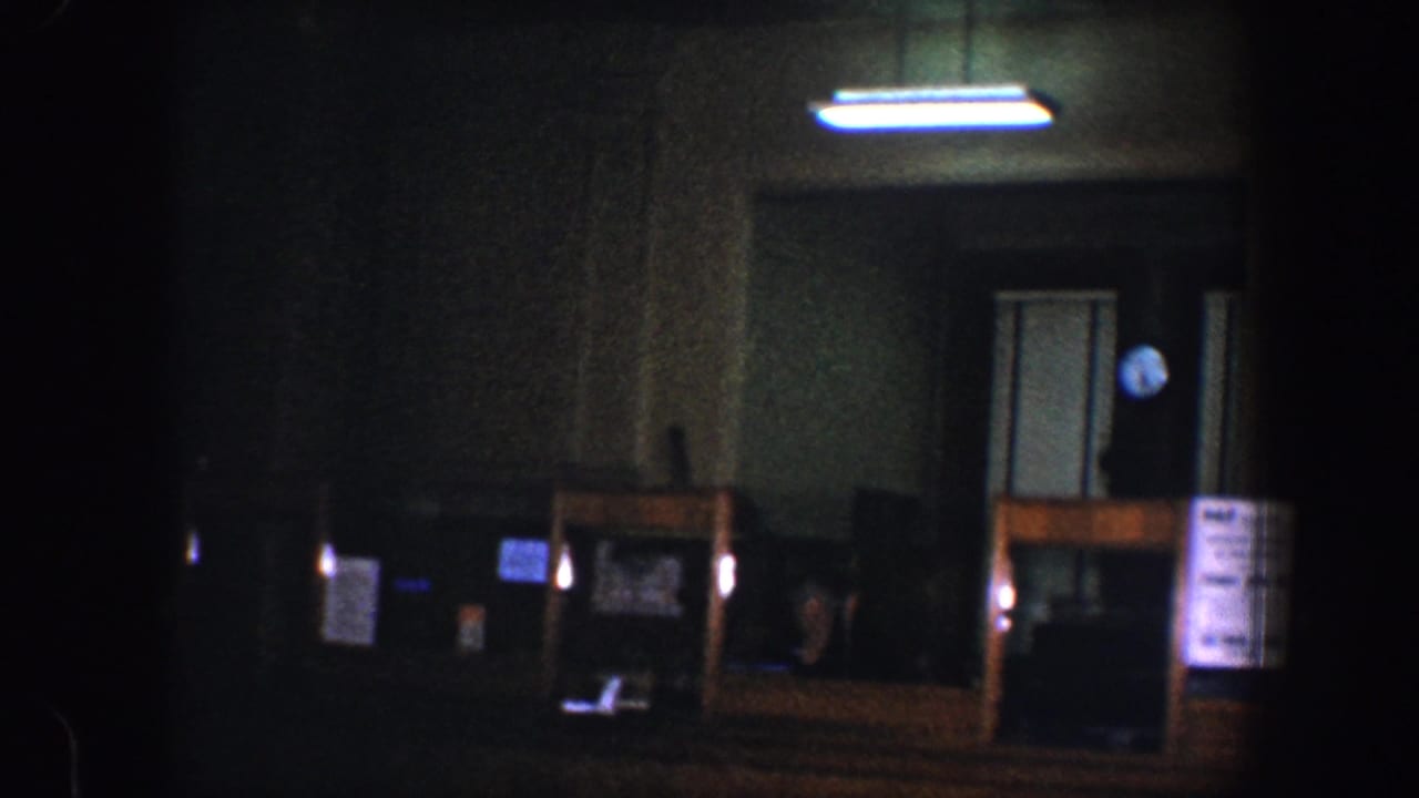 Shadowed room with doorway, fluorescent light, counter, papers, and wall clock.