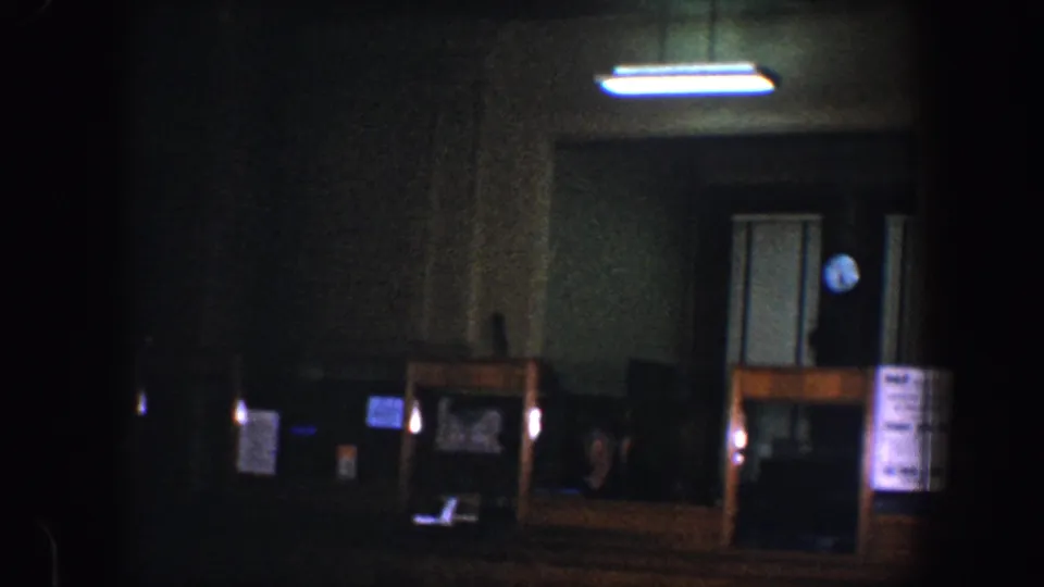 Dimly exposed 1960s Baltimore interior showing a doorway, round wall clock, counter area, and paper notices under fluorescent light.