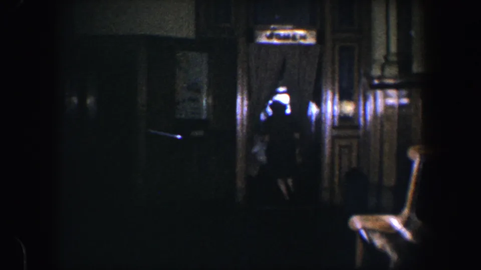 A woman moves near a curtained doorway inside a dark 1960 Baltimore residential interior with glossy wood trim and low household light.