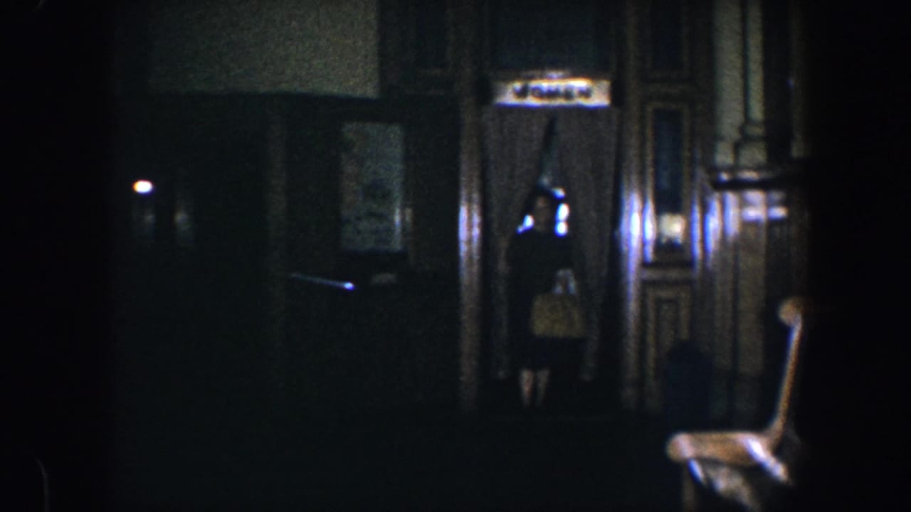 Dim hallway with a woman partly visible near a doorway and dark wood paneling.