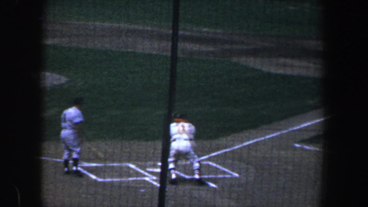 Catcher crouches behind home plate as a batter stands nearby behind netting.