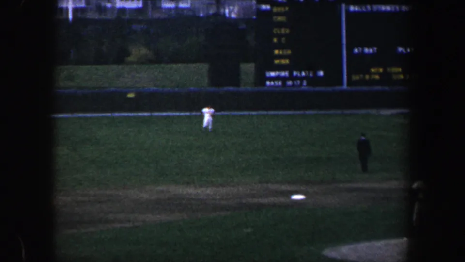 Wide 1960 Baltimore stadium view with baseball players on the field and the scoreboard partly visible at the top.