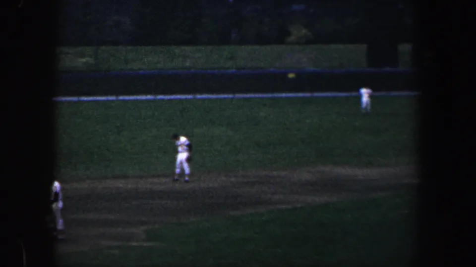 1960 Baltimore baseball scene with players in white uniforms positioned around the infield and outfield in low light.