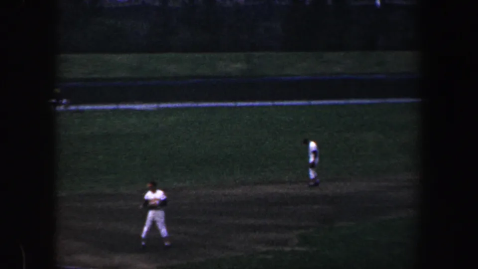 Low-light 1960 Baltimore baseball footage showing a player near the infield and another player farther across the grass.