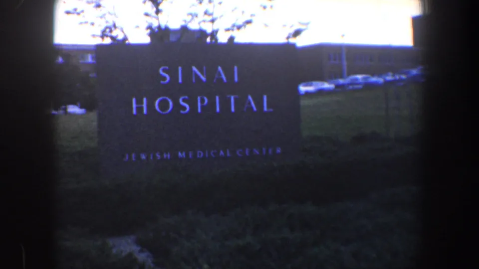 1960 Baltimore 8mm frame showing the Sinai Hospital Jewish Medical Center sign outside a low hospital building.