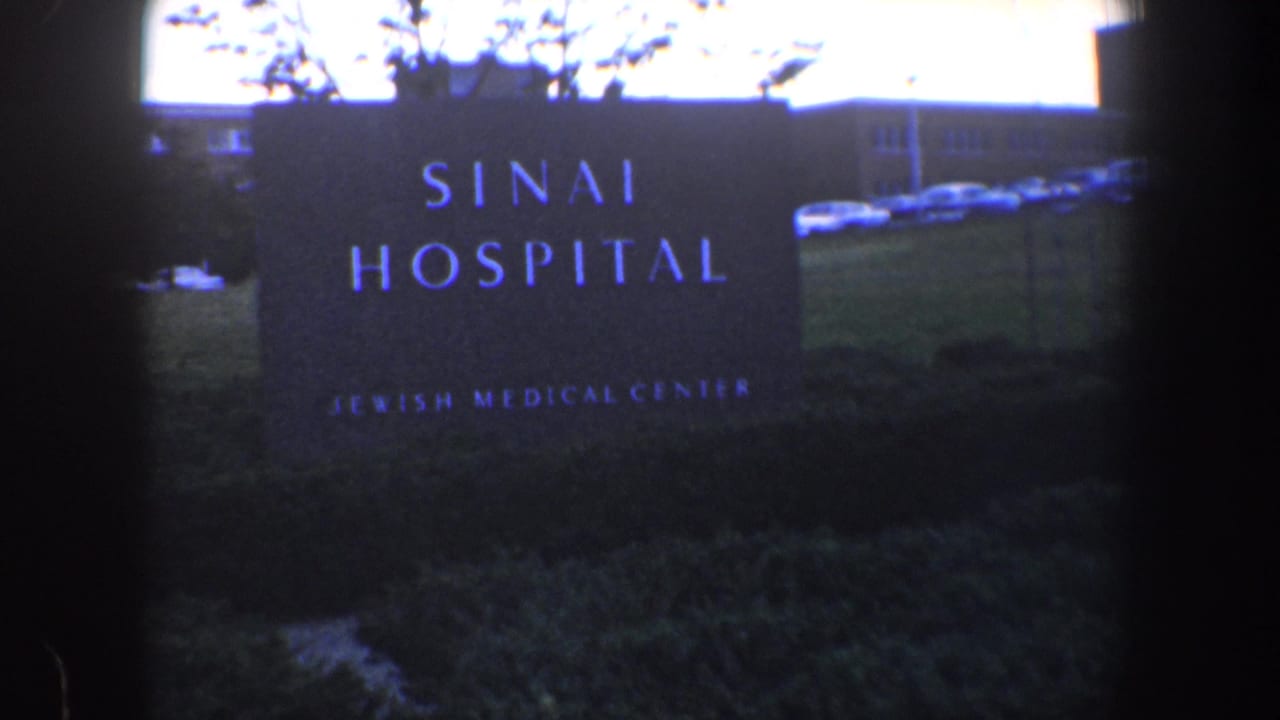 Sinai Hospital sign with parked cars and hospital building behind it.