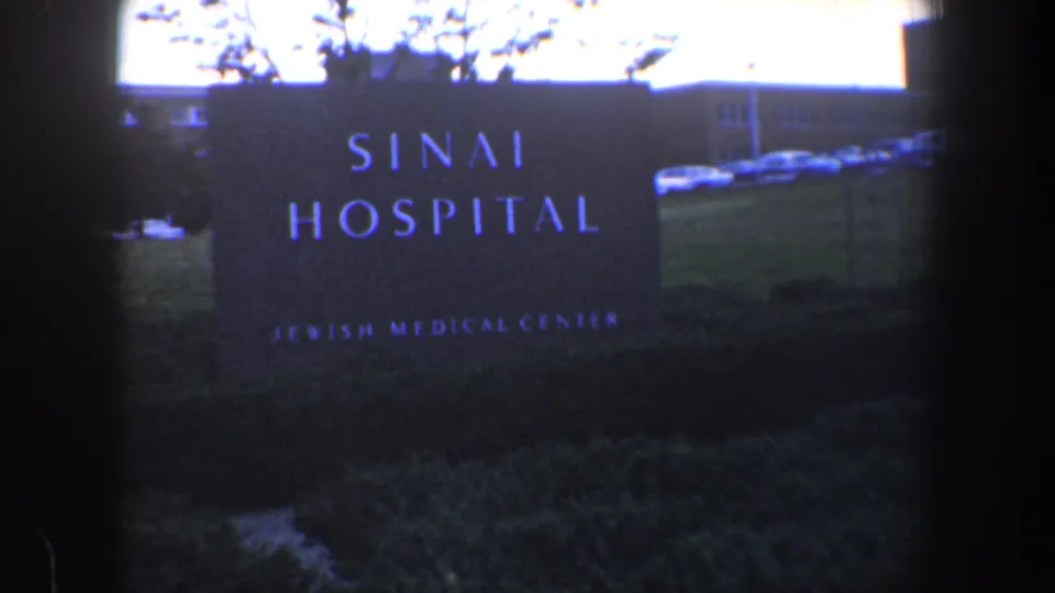 1960 Baltimore hospital exterior with the Sinai Hospital sign, lawn, parked cars, and low medical-center building.