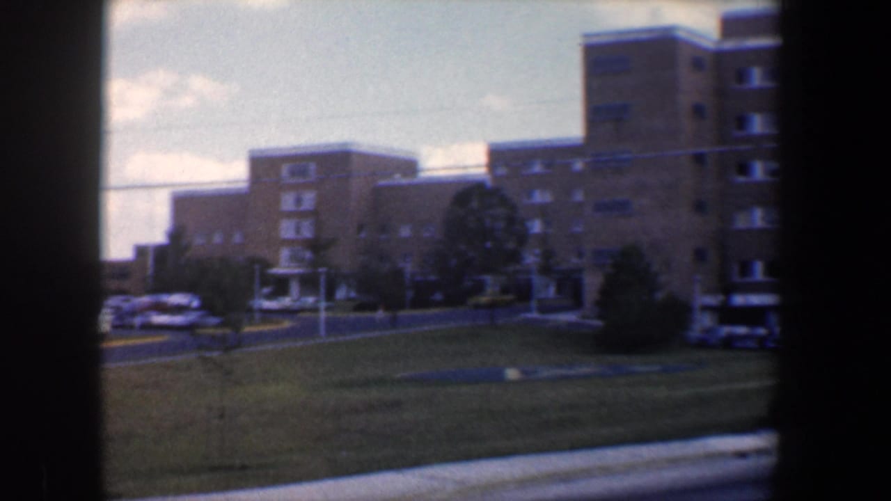 Tan brick building complex with lawn, parked cars, and dark frame borders.
