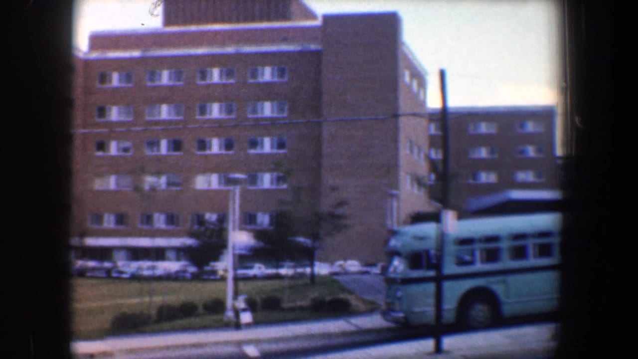 Light blue-green bus beside a brown brick building seen through dark window bars.