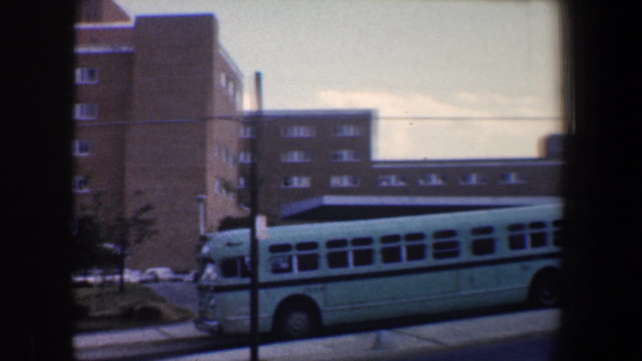 Bus moving along the curb in front of brick buildings and parked cars.