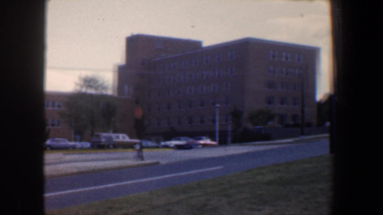Large tan building beside a road with cars parked along the curb.