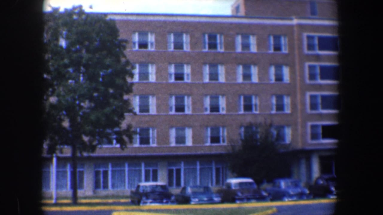 Brick multi-story building seen past dark film borders with parked cars and a tree in front.