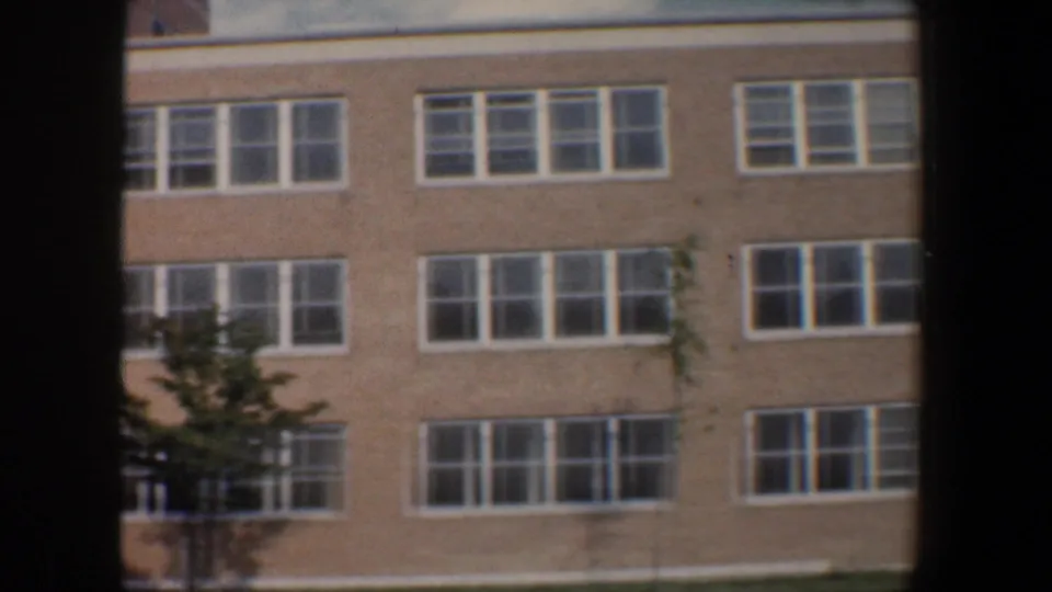 1960 Baltimore exterior view of a long tan brick building facade with repeated white-framed windows and small trees along the base.