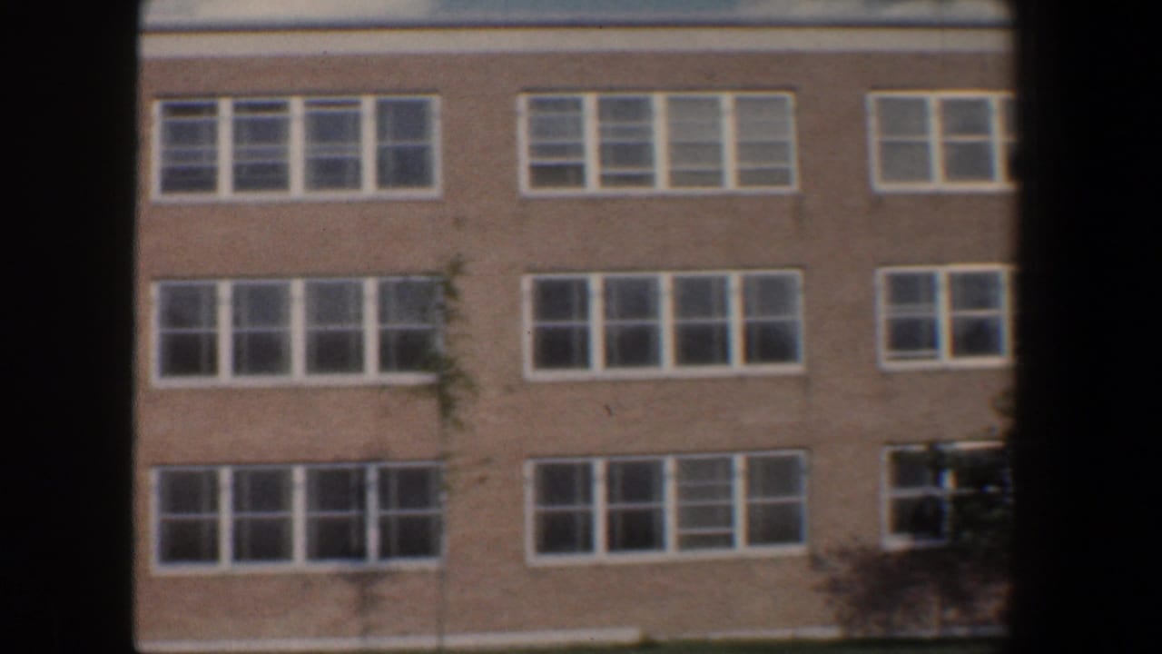1960 Baltimore 8mm view of a brick building facade with repeated white-framed windows and a small tree at the edge.