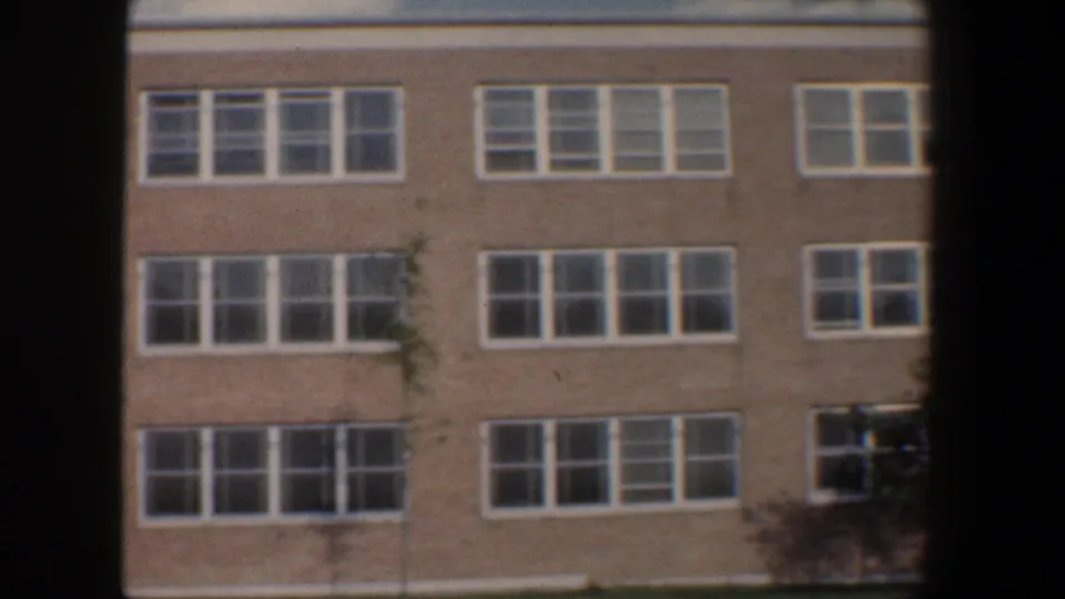 1960 Baltimore 8mm view of a brick building facade with repeated white-framed windows and a small tree at the edge.