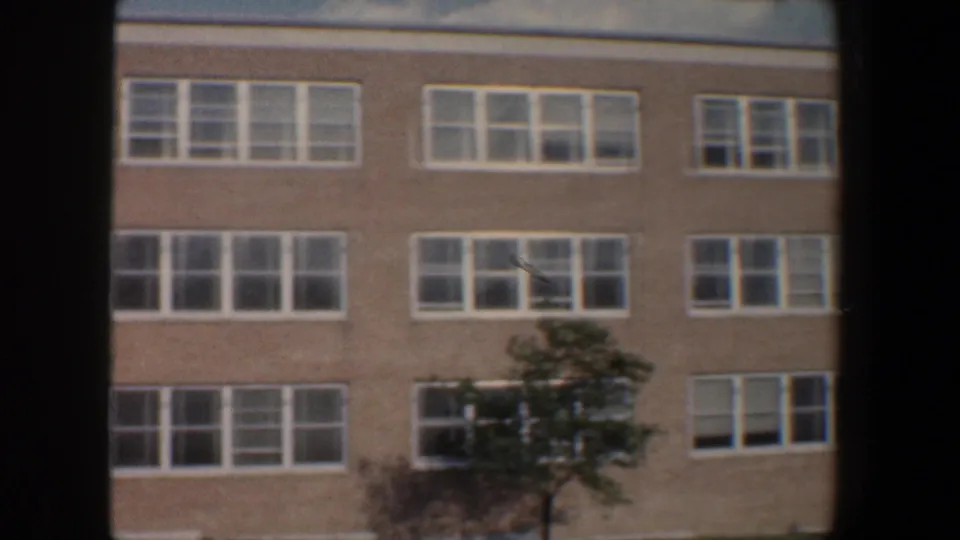 1960 Baltimore exterior view of a brick institutional-looking building with white windows and trees in the foreground.