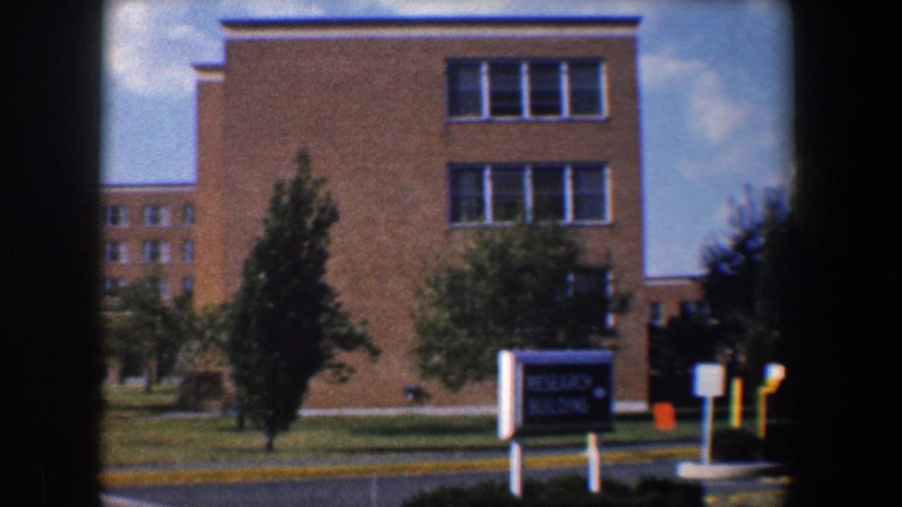 Tan brick research building seen across a lawn with a sign and trees.
