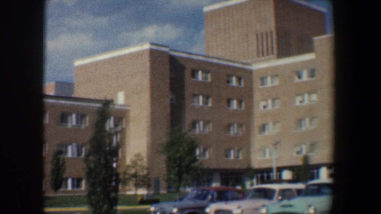 Brick apartment complex with a taller tower section and several parked cars in the foreground.