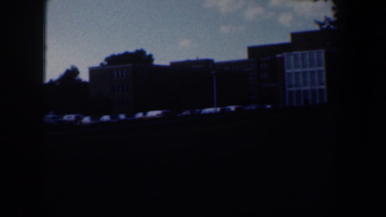 Darker view of apartment buildings and parked cars seen across a grassy foreground.