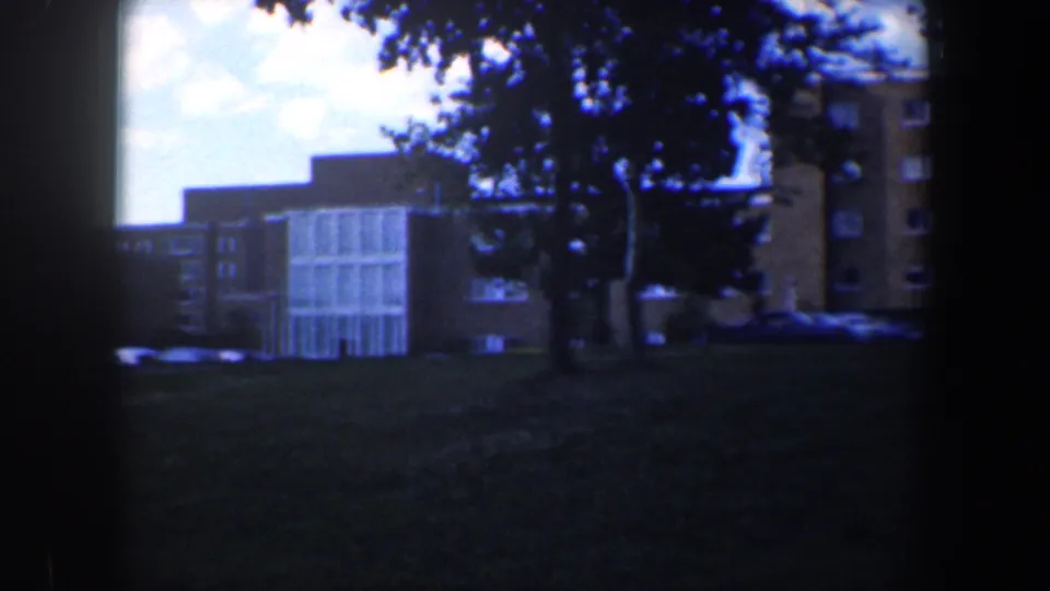 1960 Baltimore home-movie frame with trees, lawn, parked cars, and apartment buildings at the end of the pan.