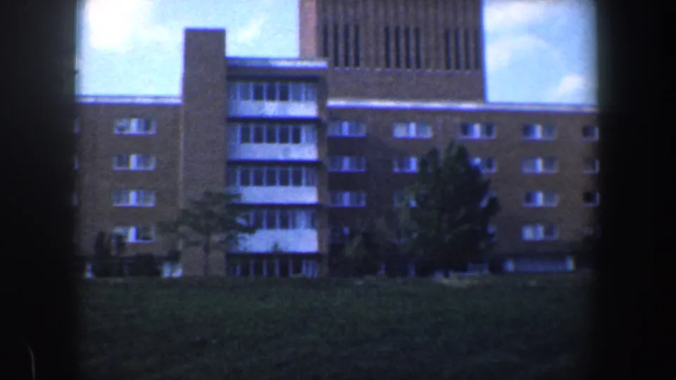 1960 Baltimore 8mm frame showing a closer portion of the brick apartment complex, including windows, balcony-like sections, trees, and grass.