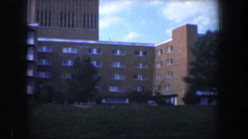 1960 Baltimore 8mm frame showing the apartment building corner, repeated windows, a lawn, trees, and dark film-gate borders.