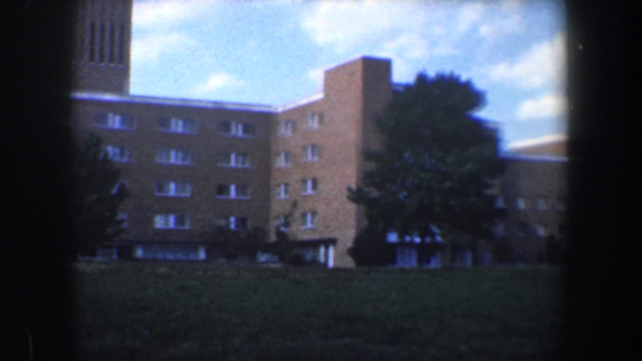 Brown brick building with tower, windows, trees, lawn, and blue sky.
