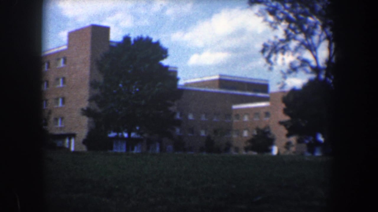 Brick building facade, trees, lawn, sky, and dark film borders during the pan.