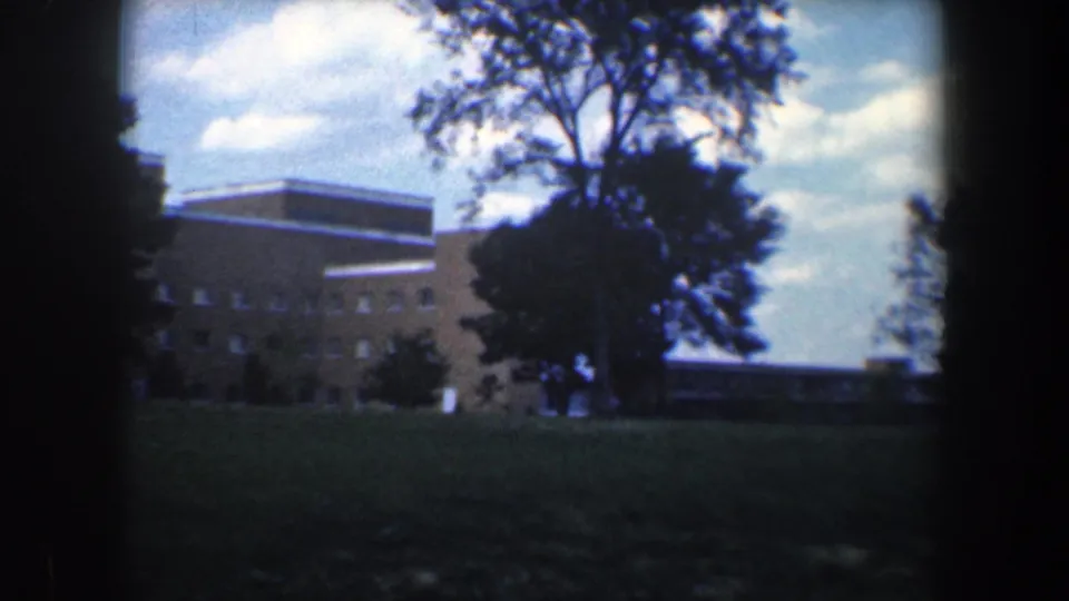 1960 Baltimore 8mm frame showing a flat-roofed brick section beside a tall tree and open grass.
