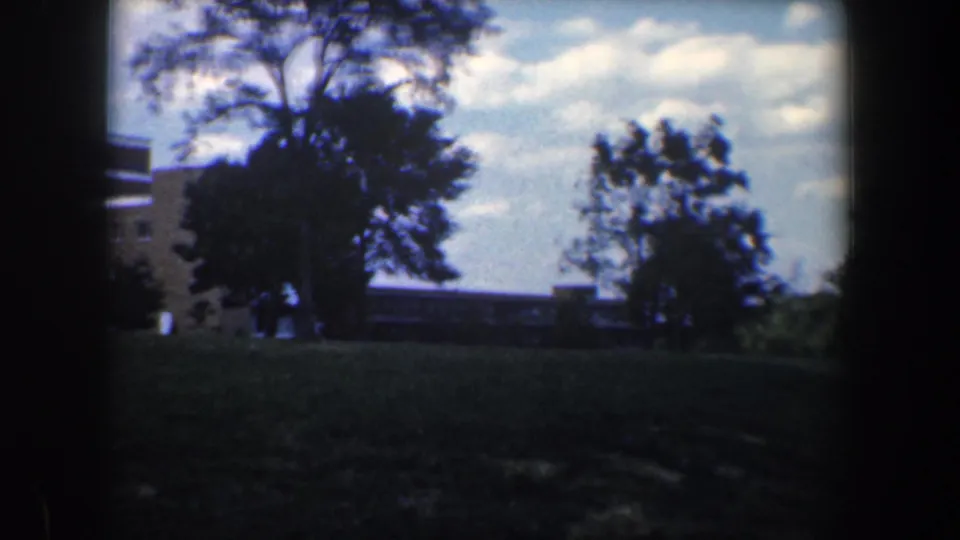 1960 Baltimore frame near the end of the pan, with trees, lawn, and a lower building section in view.