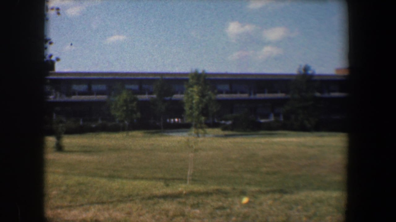 Campus field with small trees and a low building seen through dark frame edges.