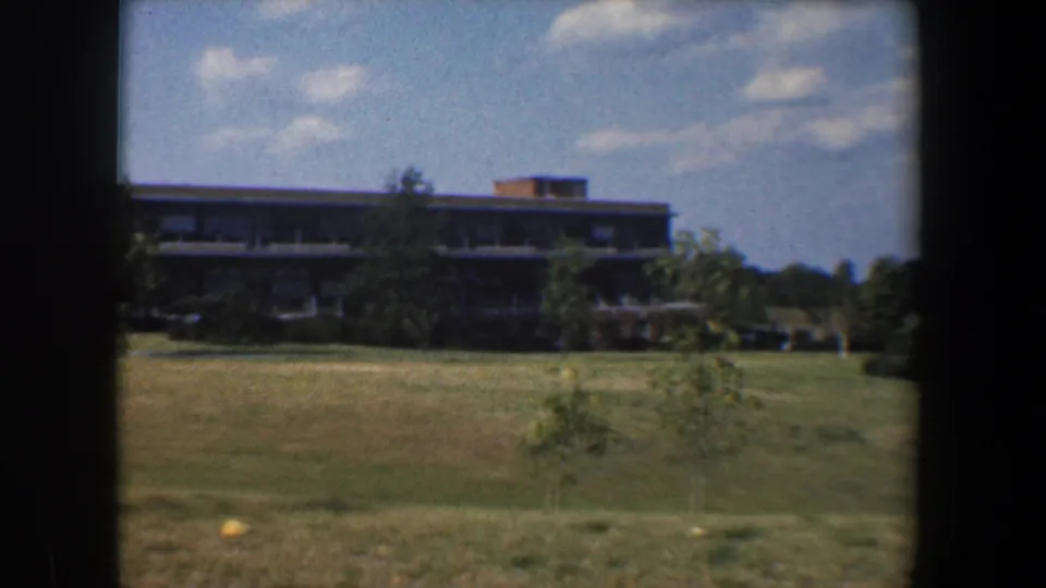 Late shot of the 1960 Baltimore campus view, with open lawn, young trees, distant modern building and soft 8mm color.
