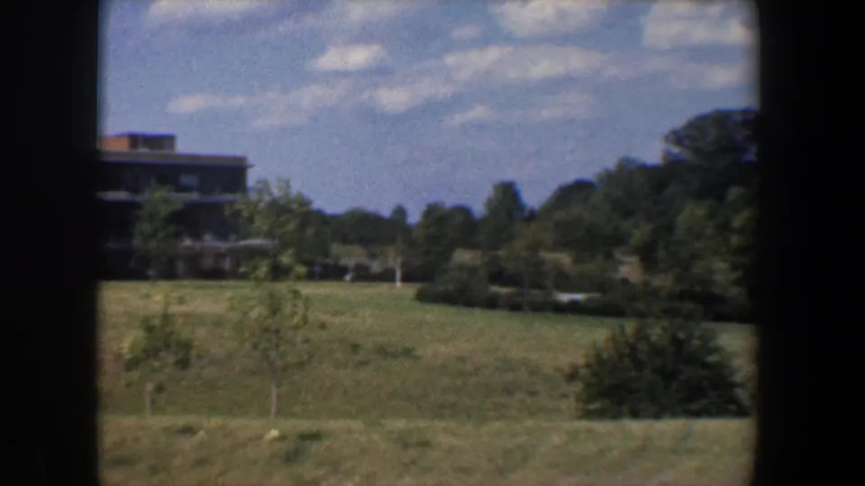 The pan continues across a Baltimore-area grassy landscape, with scattered trees and a partial distant building visible at the left edge.