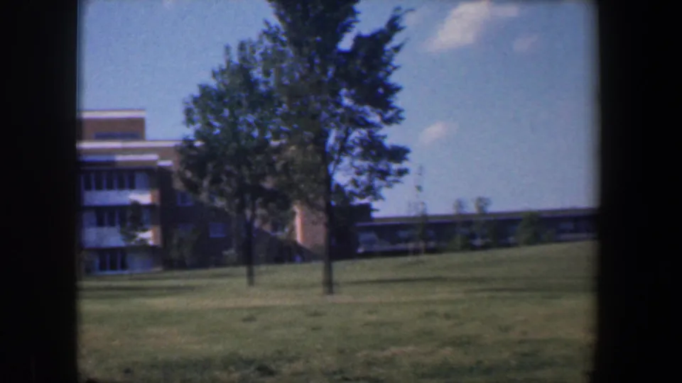 1960 Baltimore 8mm view of a brick public or institutional building behind trees and an open lawn.