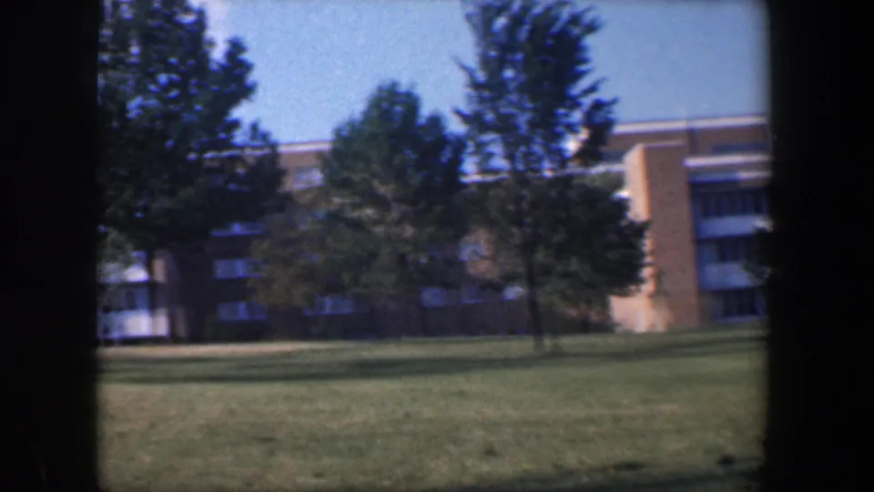 1960 Baltimore 8mm frame showing a brick building facade, trees, and a broad lawn.