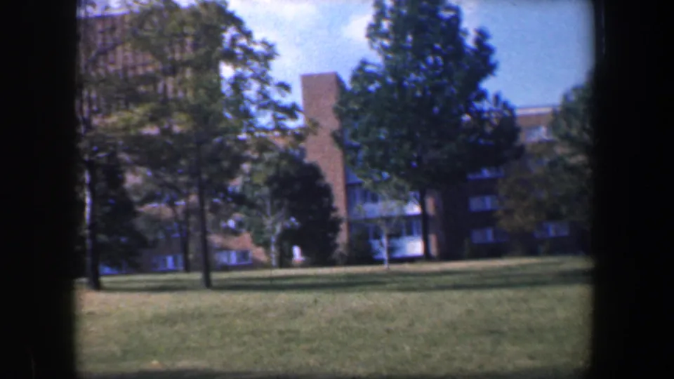 1960 Baltimore home-movie frame of trees and lawn before a brick public building exterior.