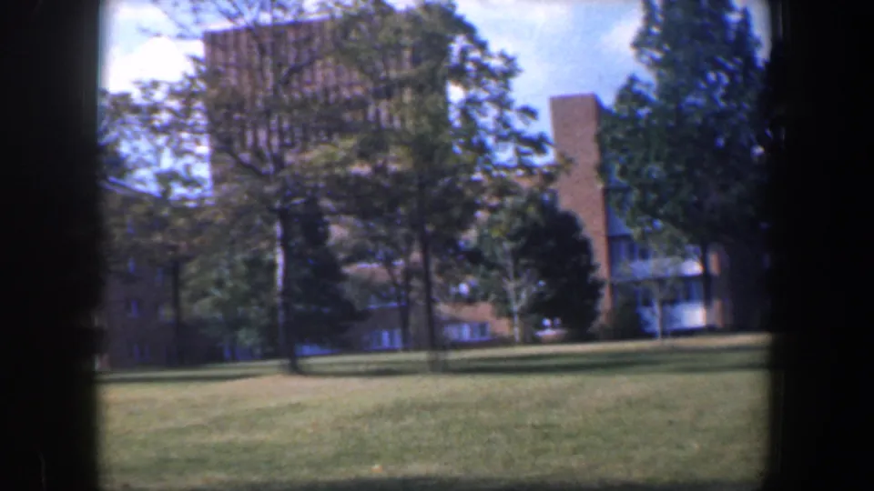 1960 8mm view in Baltimore of brick institutional buildings, trees, and a broad lawn in bright daylight.