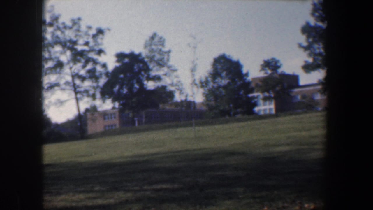 Distant tan brick buildings across a grassy slope with trees and dark film borders.