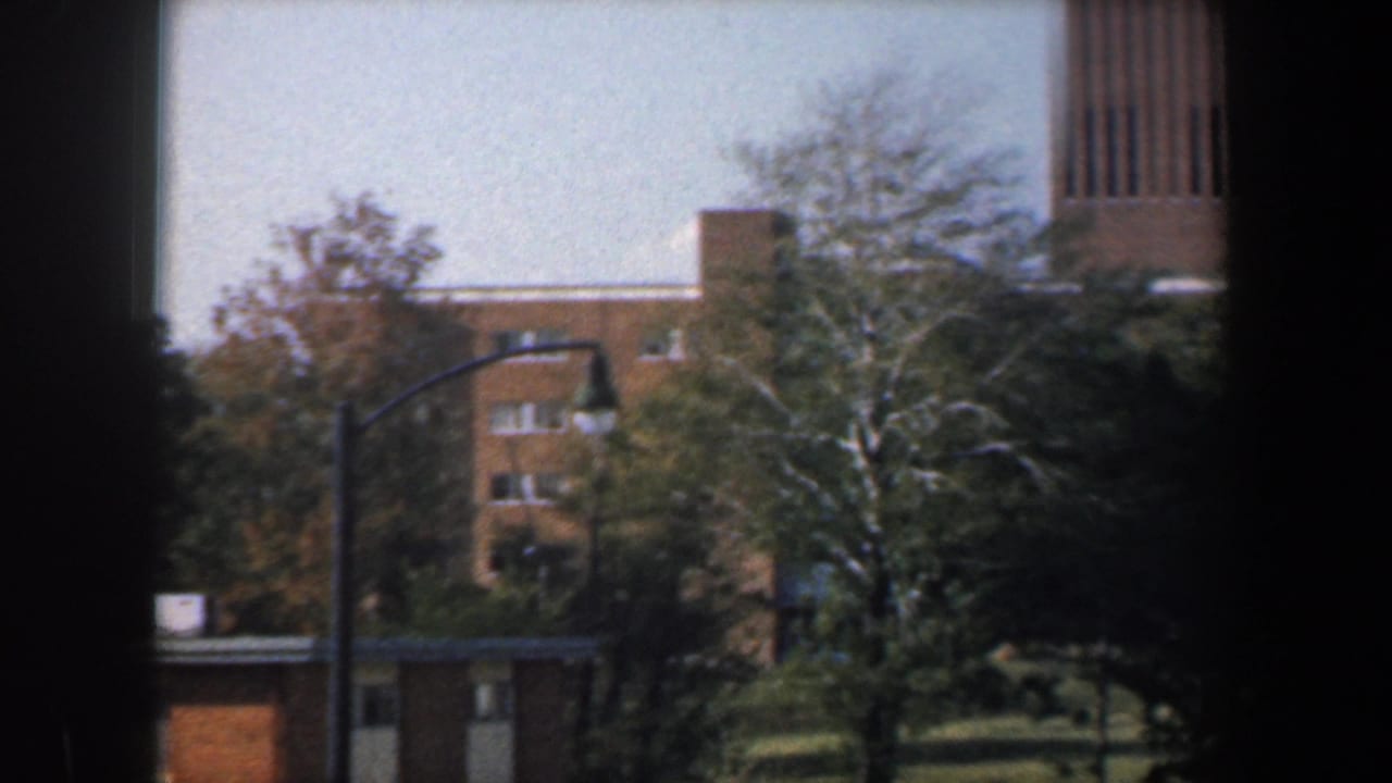 Tan brick apartment buildings seen through dark window framing with trees and a street lamp in front.